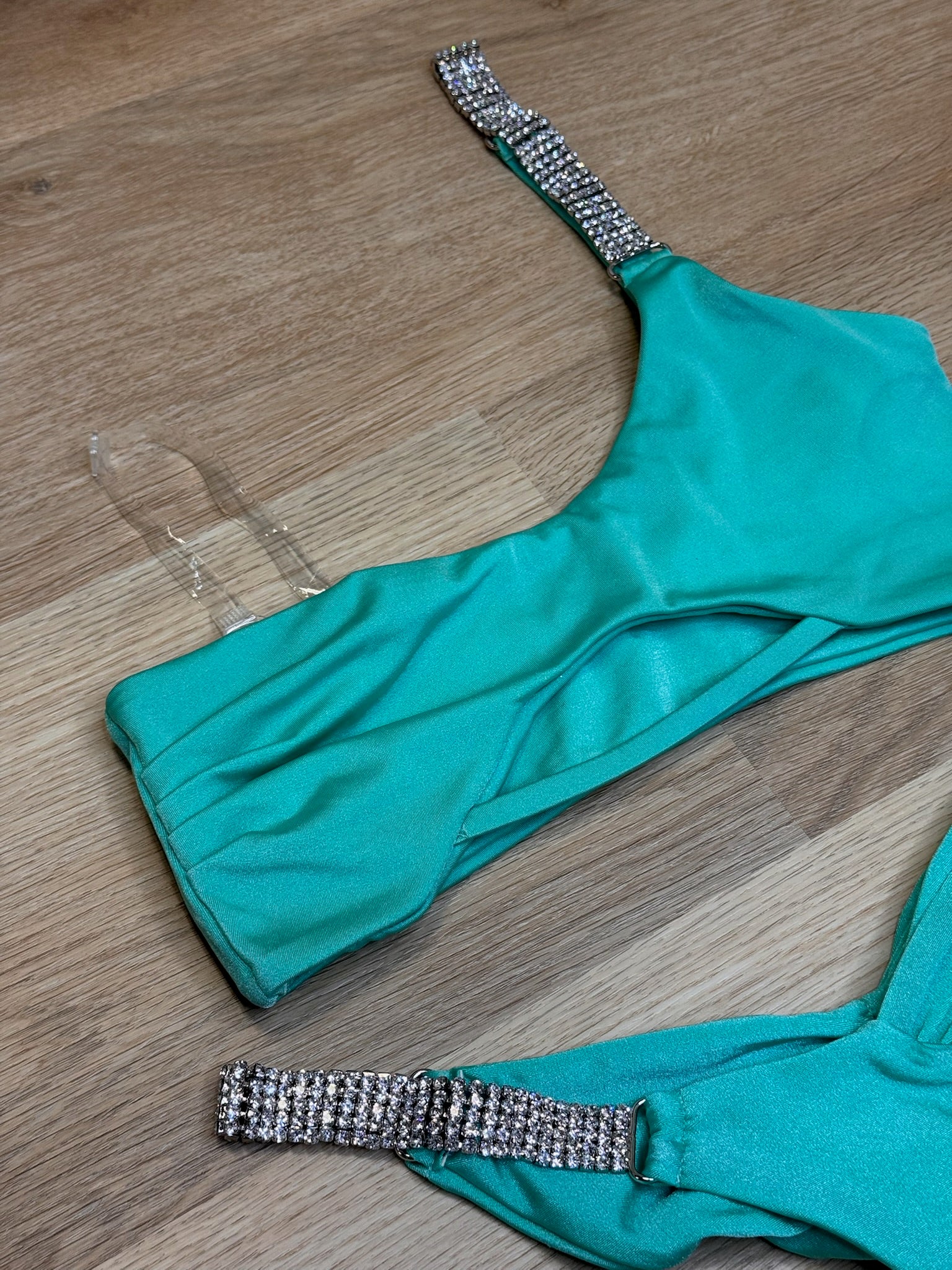 Teal bikini top with rhinestone straps on a wooden surface
